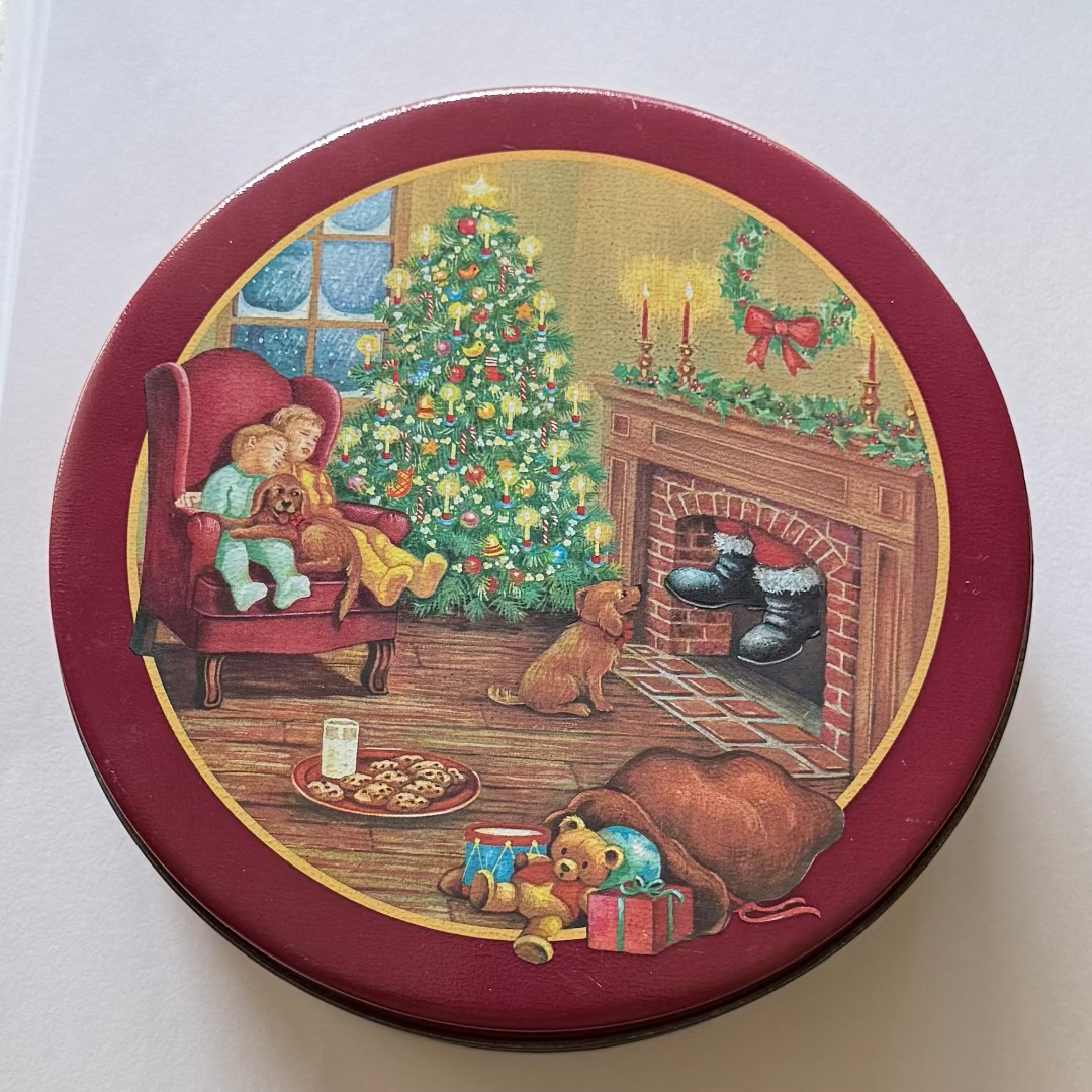 Decorative Christmas tin with a festive scene of children, dogs, and a fireplace.