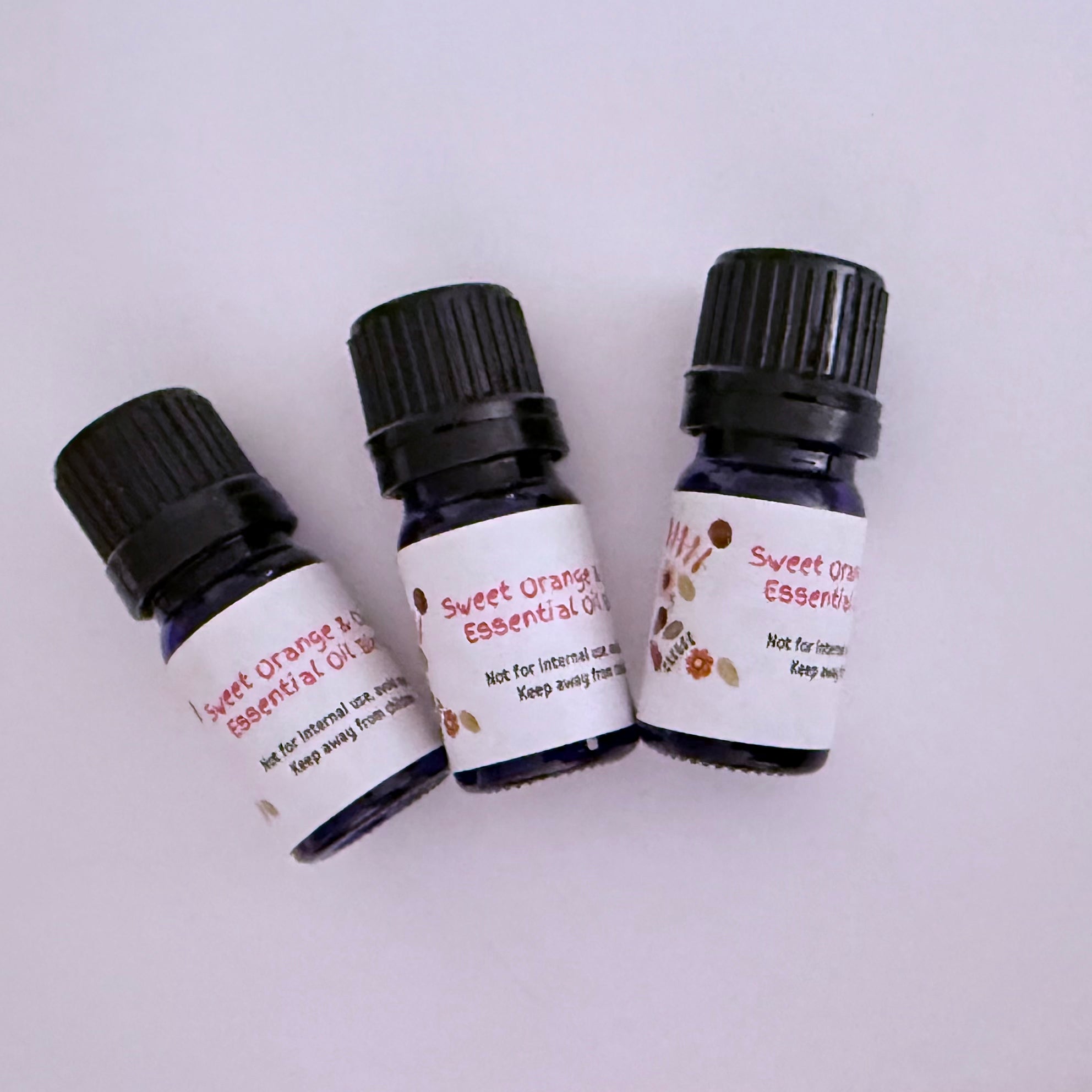 Three bottles of Sweet Orange and Clove  Essential Oil Blend by Aroma Thyme with black caps on a white background